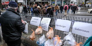 Ein Mann steht vor einem Zaun, an dem Plastiktüten hängen. Darüber hängen Schilder "Hamburger Gabenzaun".