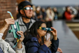 Besucher des Hamburger Planetariums betrachten von der Aussichtsterasse aus mit Schutzbrillen eine partielle Sonnenfinsternis.