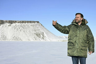 Mann in Winterjacke vor Schneekulisse zeigt in eine Richtung