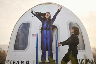 Eine Frau mit langen schwarzen Haren und in einem blauen Anzug (Amanda Nguyen) steigt jubelnd aus einem Flugzeug.