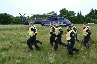 Polizisten laufen über eine Wiese, im Hintergrund ein Helikopter